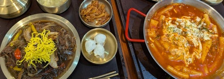 Korean meal with cold noodles, fried chicken, rice cakes in spicy sauce, soup, and side dishes on a table